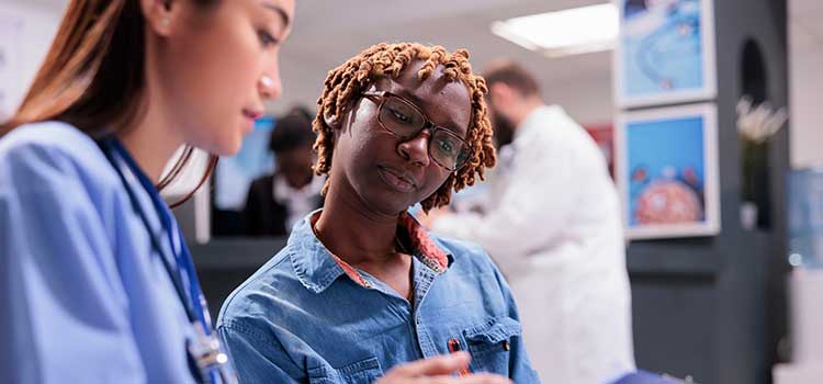 medical assistant works with female patient to take insurance information on chart