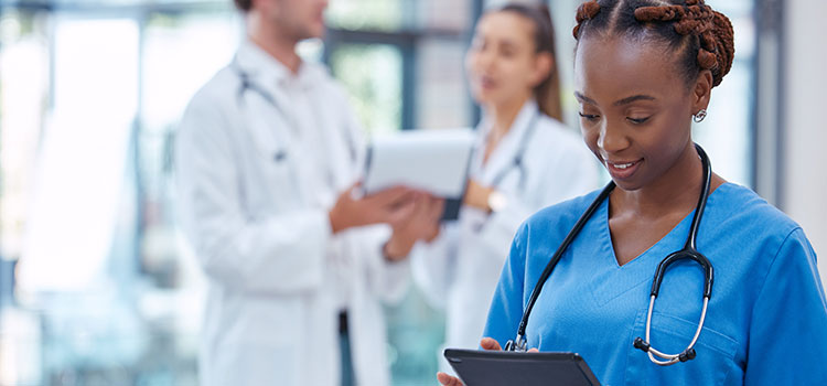medical assistant in corridor of busy clinic recording patient notes in tablet